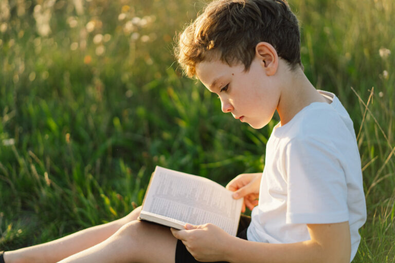 boy is reading the Holy Bible in a field during beautiful sunset