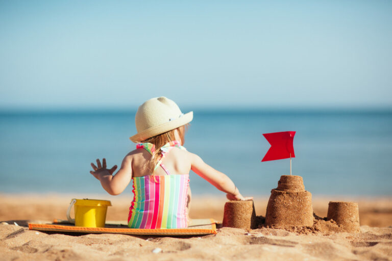 baby child in hat sits on beach against background of sea and plays sand