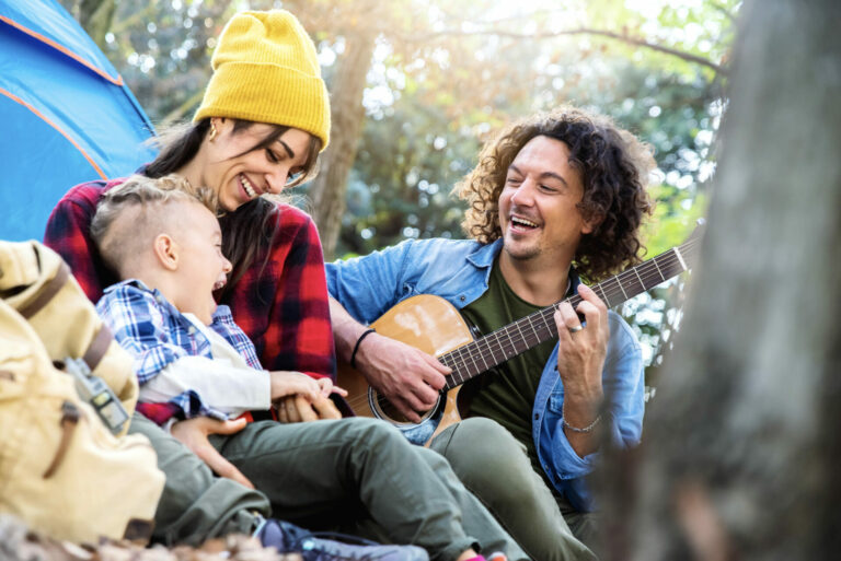 Happy family camping in the forest playing guitar and singing together