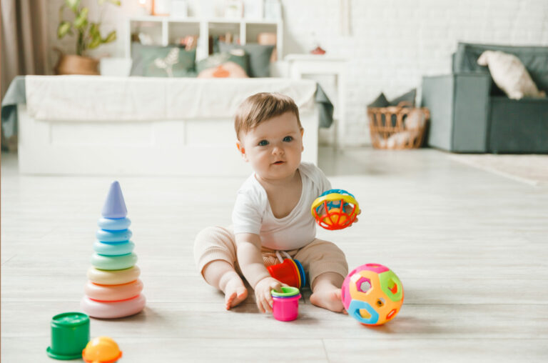 Baby playing with a colorful rainbow toy pyramid sitting in a white sunny bedroom. Toys for small children. Children's interior. A child with an educational toy.