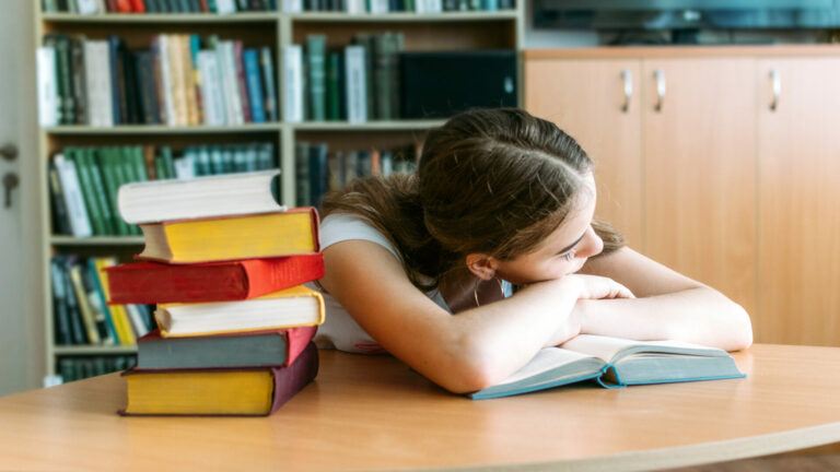 College Students overwhelmed, overworked, burned out, perfectionists. Teen tired girl, young woman sitting at table with books in college library.